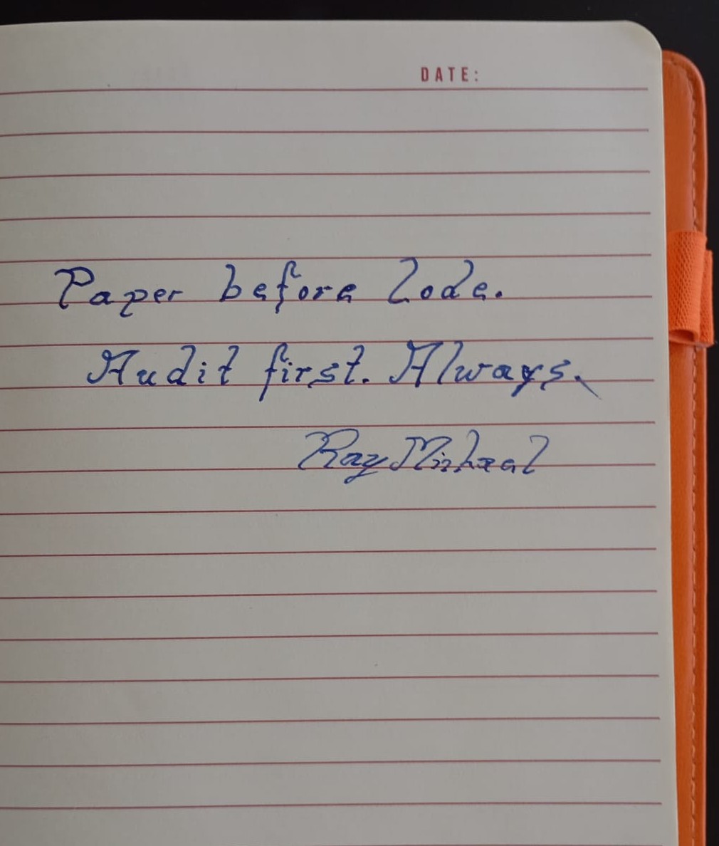 Ein offenes Notizbuch mit der in blauer Tinte geschriebenen Aufschrift „Papier vor Code. Zuerst prüfen. Immer.“; ein orangefarbener Stift liegt quer über die Seite.